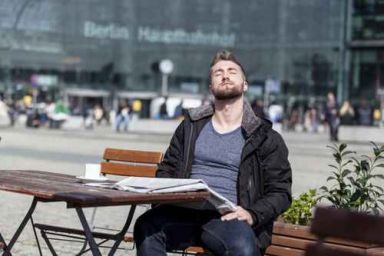 Attraktiver Mann sitzt in einem Cafe und geniesst die Sonnenstra